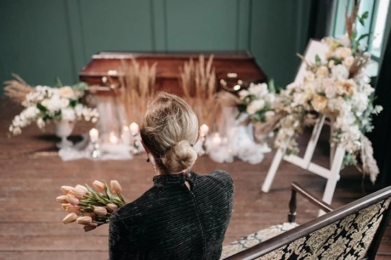 Femme de dos recueillie devant un cercueil fleuri lors d'obsèques